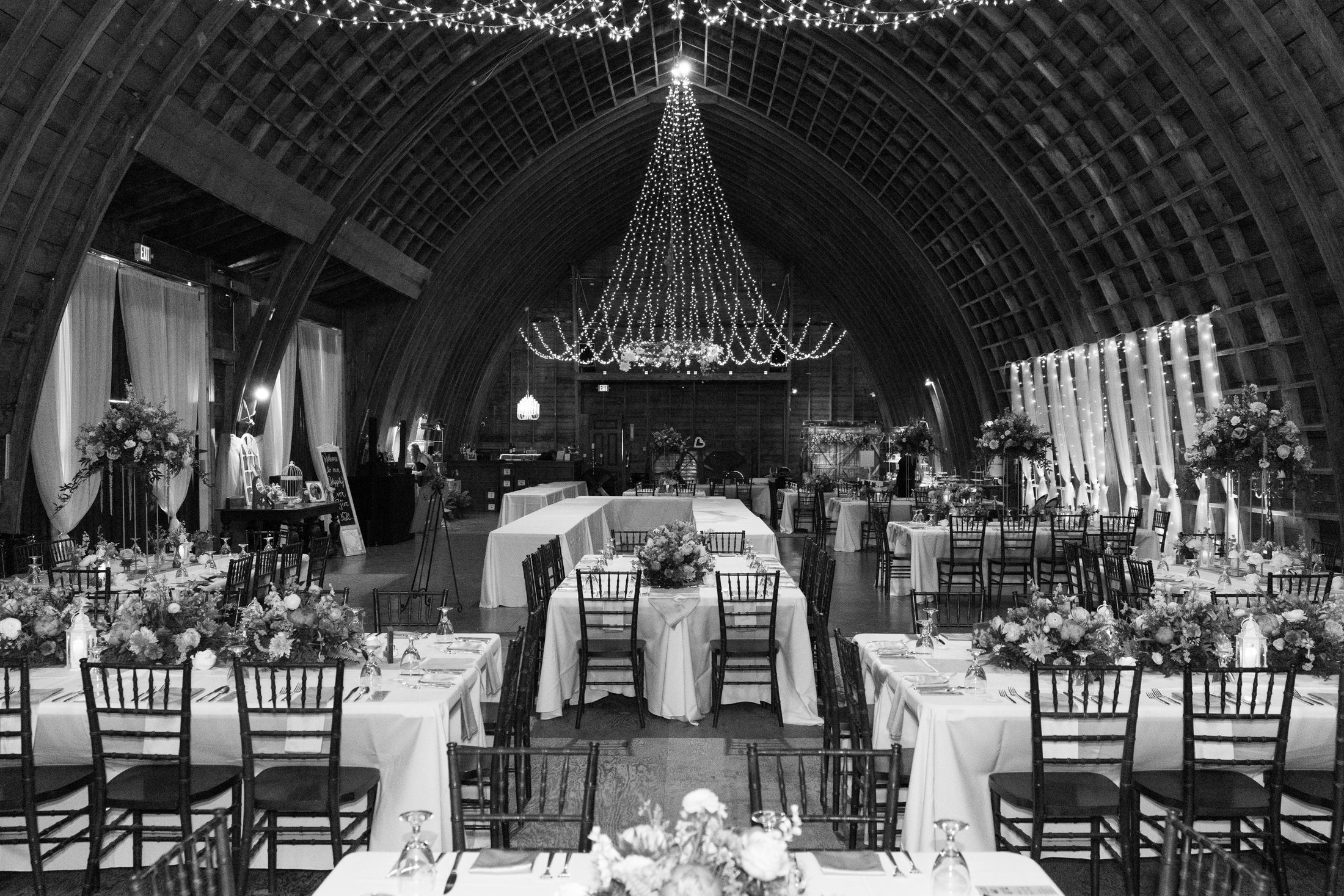A barn reception set before the guests arrive, strings of lights overhead, in black and white